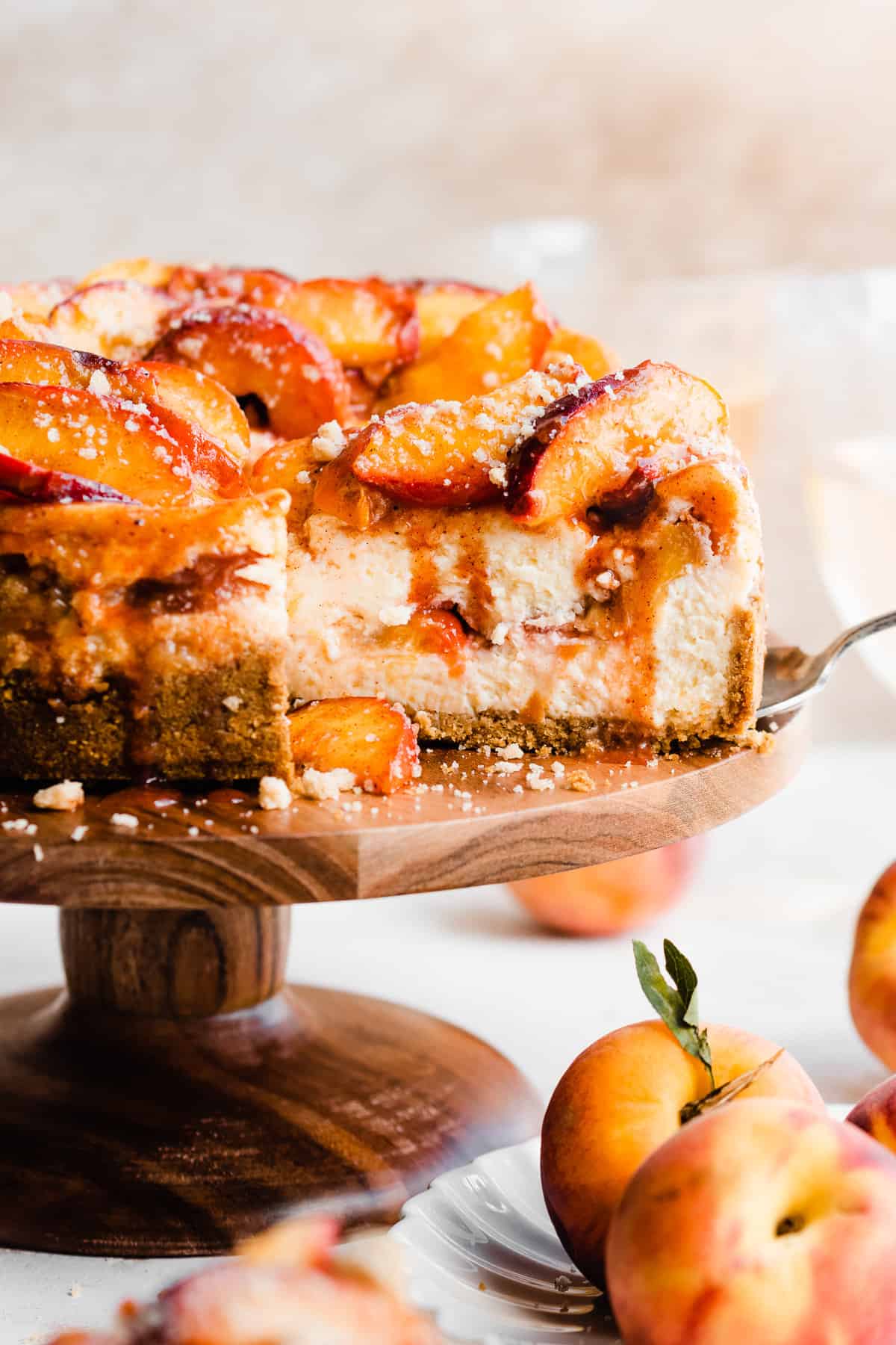 The peach cobbler cheesecake on a cake stand with a cross section cut. Juicy peach slices are on top with cinnamon peach juice dripping down.