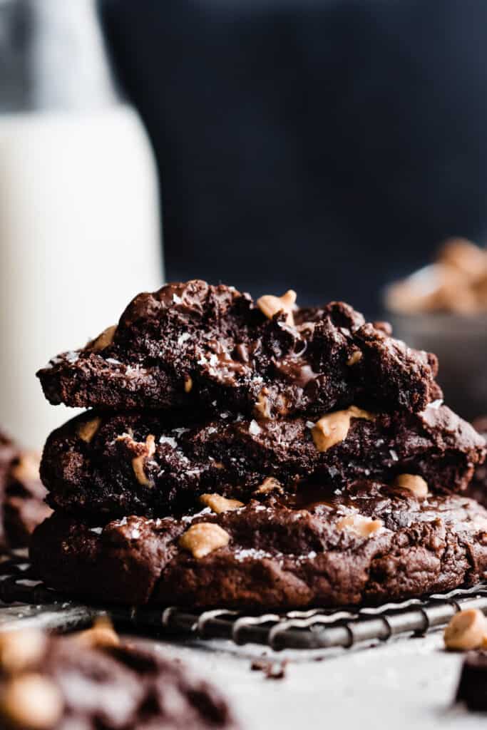 A stack of fudgy chocolate peanut butter chip cookies with the insides visible and a bottle of milk in the background.