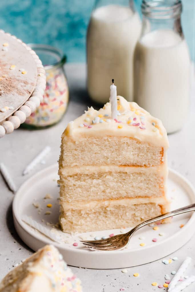 A 3/4 angle shot of a slice of cake on a plate, with a birthday candle and sprinkles on top.