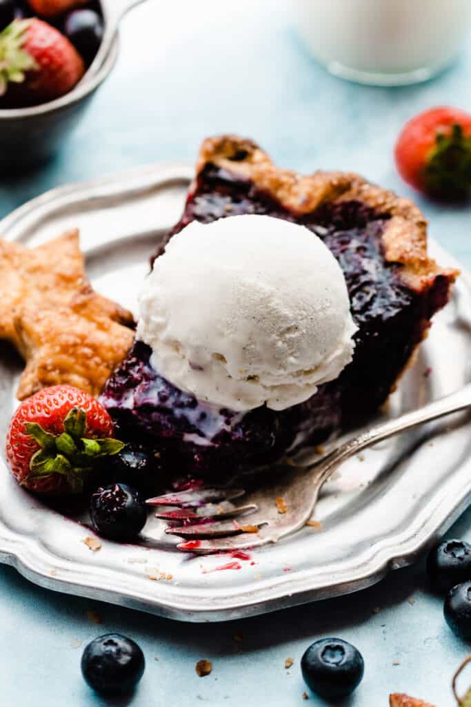 A slice of pie on a vintage silver plate, topped with a scoop of ice cream and pie crust stars. 