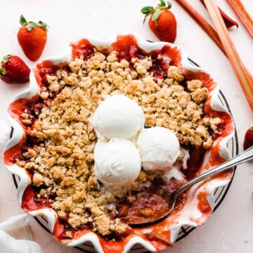 Strawberry rhubarb crumble in a pie dish topped with scoops of ice cream.