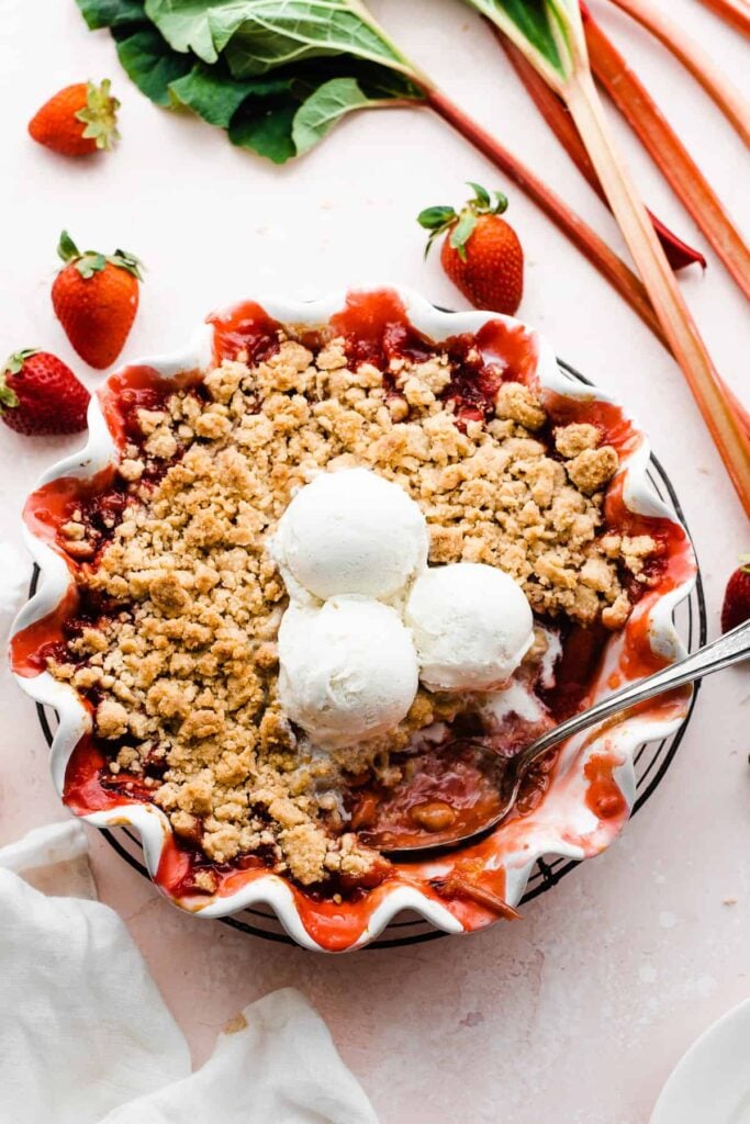 Strawberry Rhubarb crumble in a pie dish with strawberries and rhubarb scattered around.