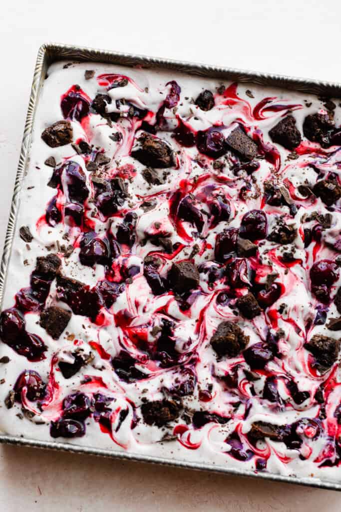 A square pan of black forest ice cream topped with cherry sauce, brownie chunks, and chocolate chunks.