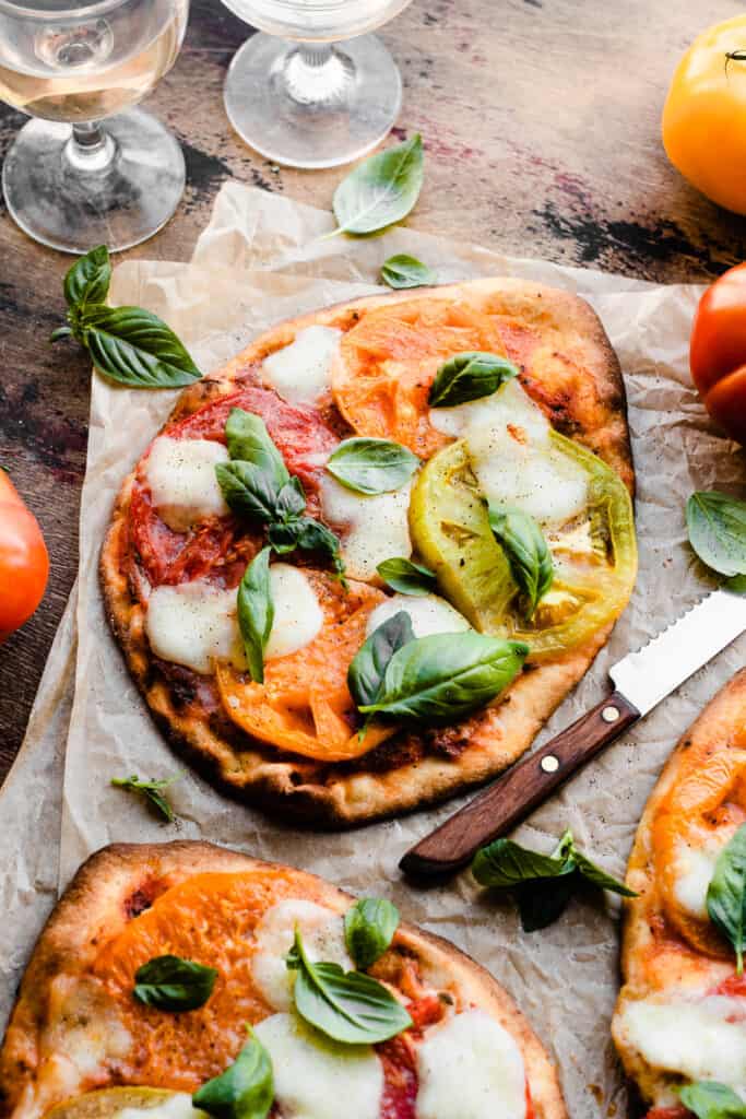 Margherita flatbread pizzas topped with heirloom tomatoes and fresh basil on a wooden surface.