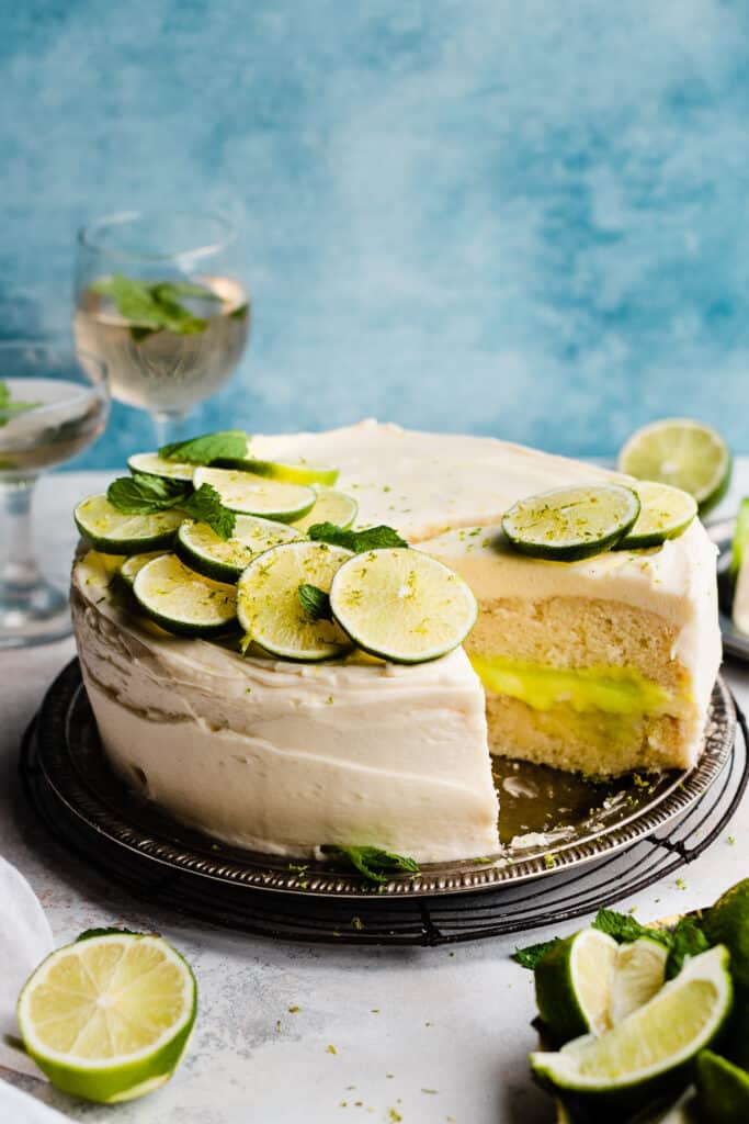 A sliced mojito cake topped with fresh lime slices and mint, on a blue backdrop.