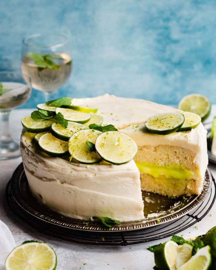 A sliced mojito cake topped with fresh lime slices and mint, on a blue backdrop.