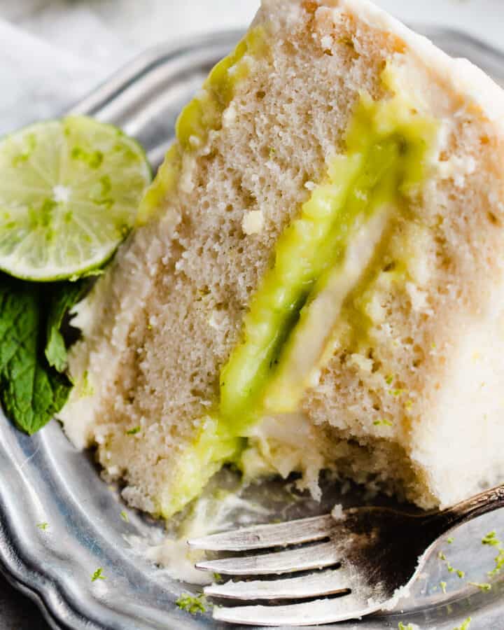 A close-up on a slice of mojito cake with visible lime curd filling, fluffy cake layers, and whipped frosting.