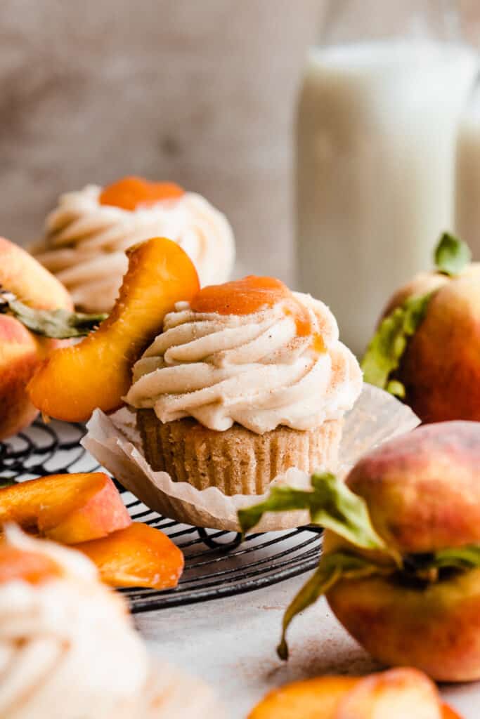 Peach cupcakes on a vintage wire rack with cinnamon cream cheese frosting and peach filling and a fresh peach slice on top.