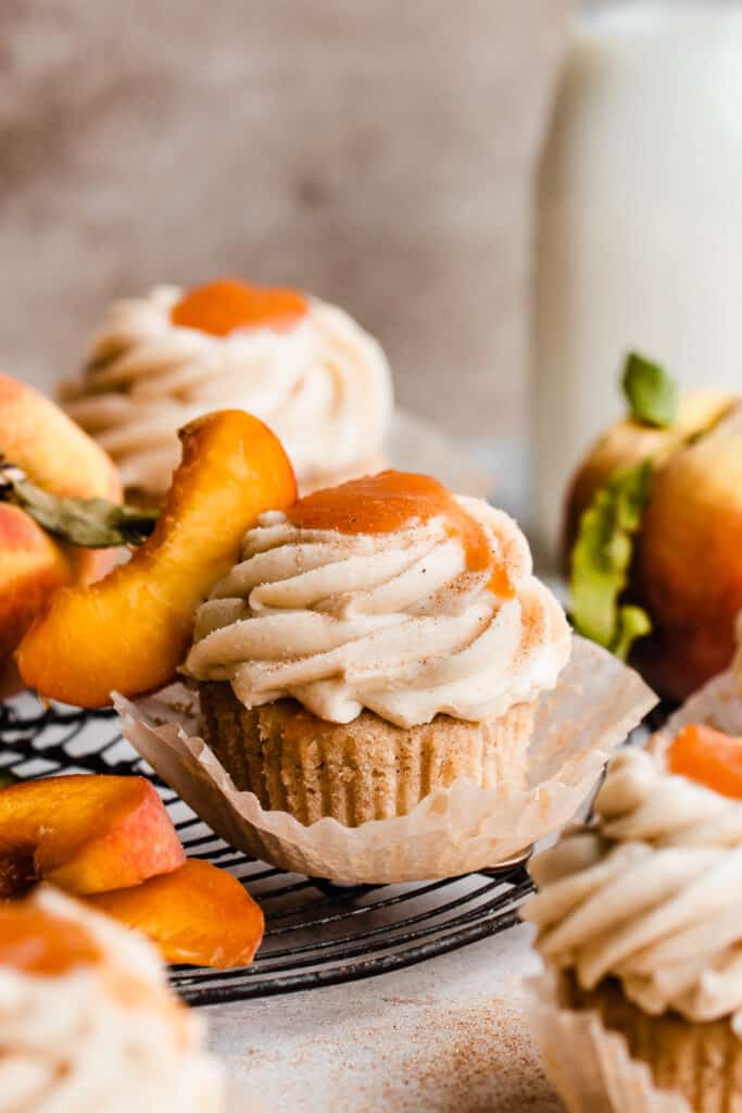 Peach cupcakes topped with silky frosting and peach filling on a vintage wire rack. 