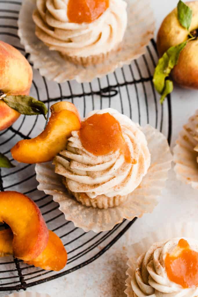 A birds eye view of the peach pie cupcakes on a wire rack, topped with frosting and a dollop of peach pie filling.