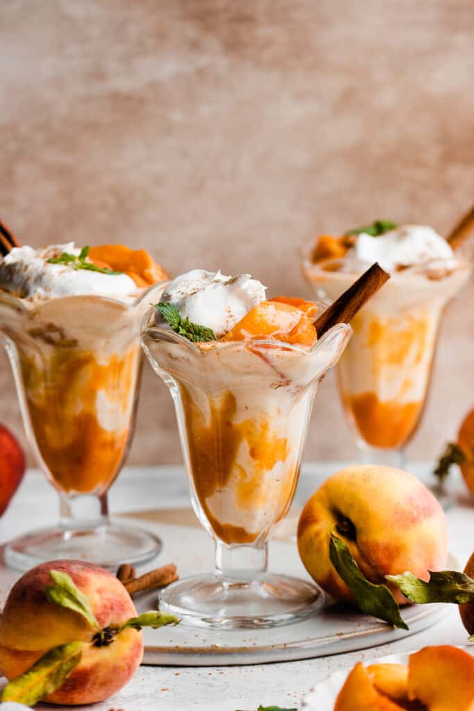 Three peach milkshakes in old fashioned glasses topped with whipped cream and a cinnamon stick.