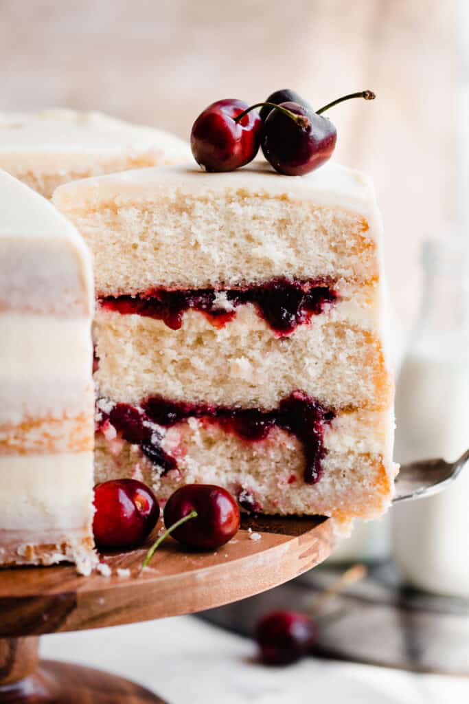 A close-up on a slice of the cake with layers of white chocolate ganache and cherry sauce inside.