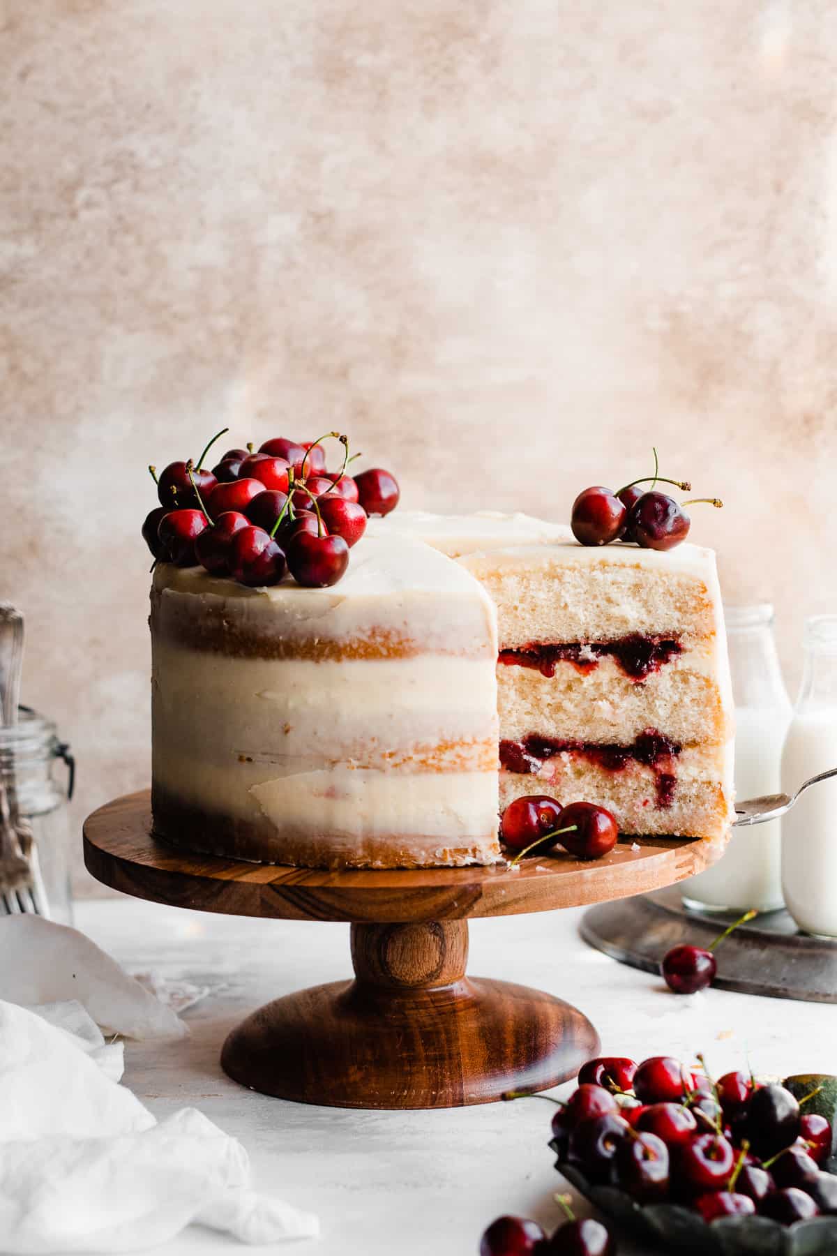 A three layer white forest cake with slices cut, showing layers of white chocolate ganache and cherry sauce.