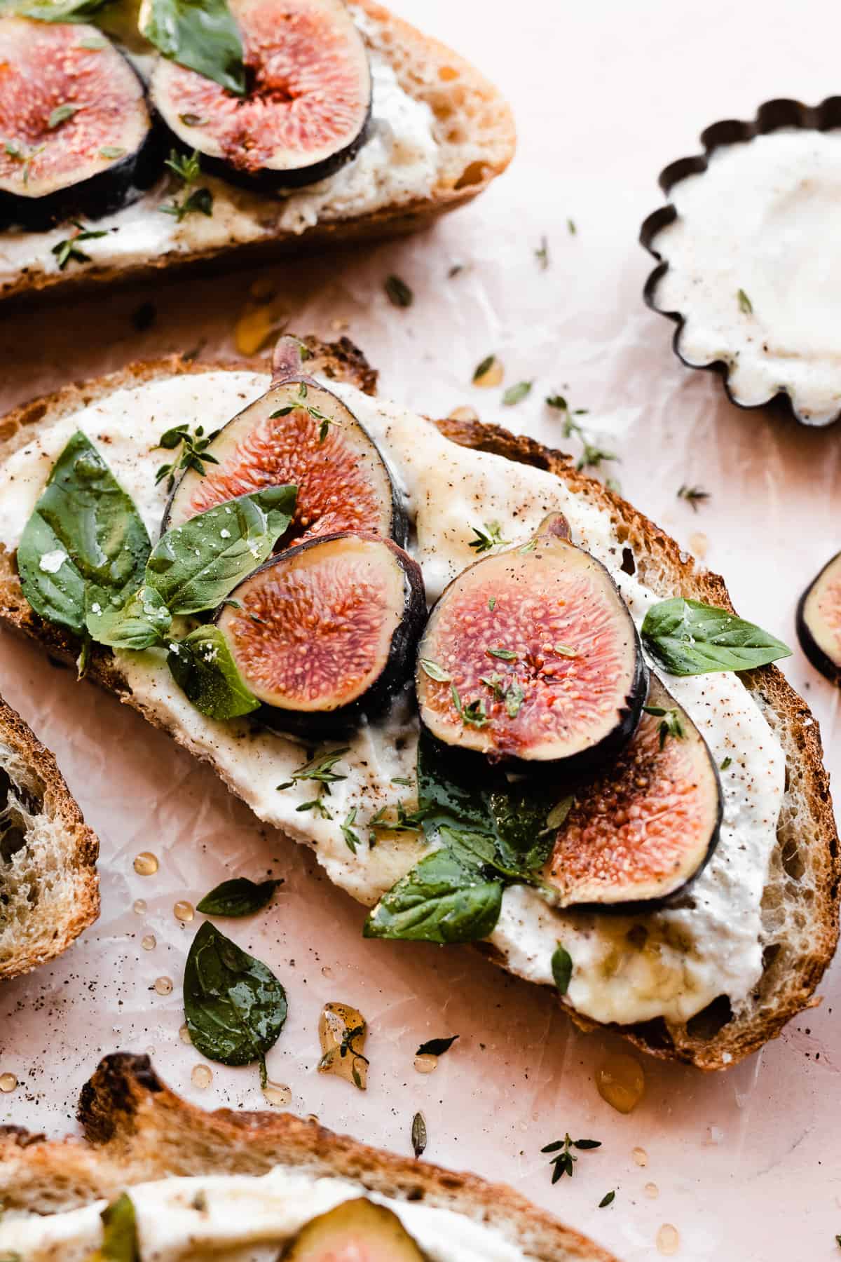 A close-up on a slice of ricotta toast topped with figs, basil, and honey.
