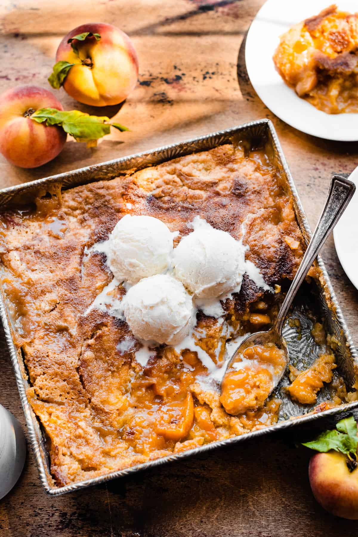 Cake mix peach cobbler in a baking dish with vanilla ice cream on top.