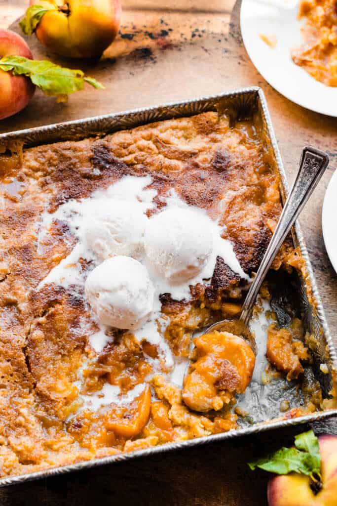 The pan of cake mix peach cobbler with ice cream melting on top.