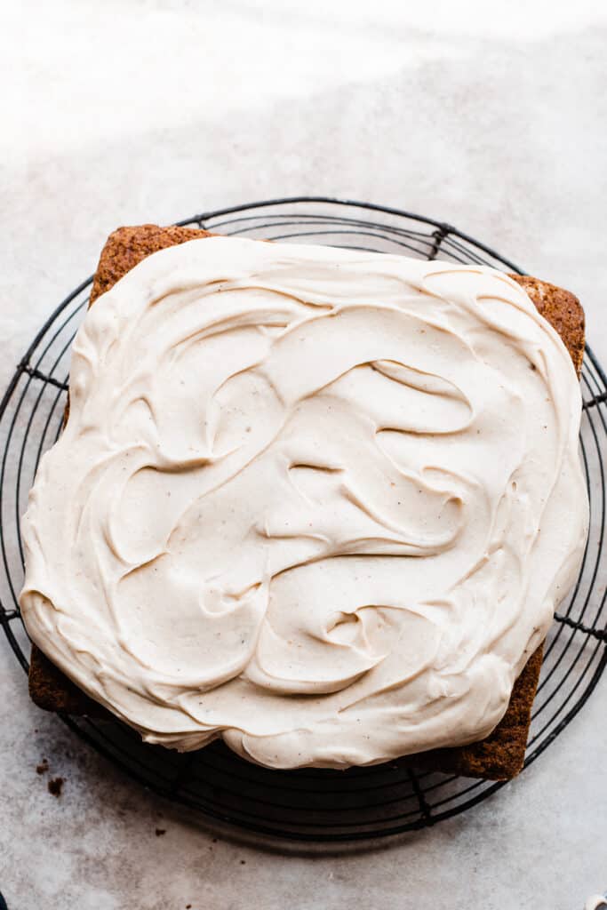 Banana cake topped with swirls of maple frosting on a cooling rack.