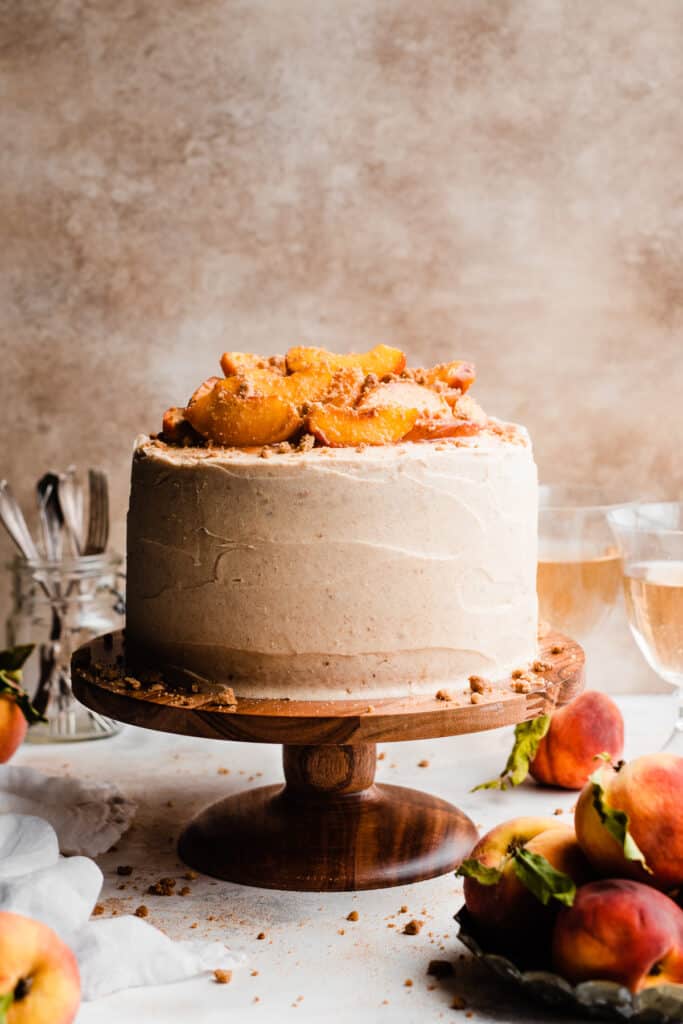 The full peach cobbler cake topped with roasted peaches on a cake stand.