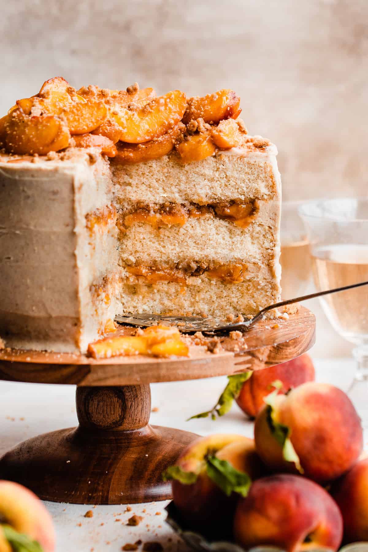 A sliced peach cobbler cake on a cake stand with visible layers of brown butter frosting, peach filling, and streusel.