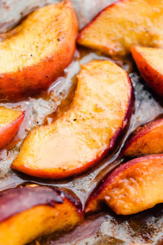 A close-up of roasted peaches on a baking sheet.
