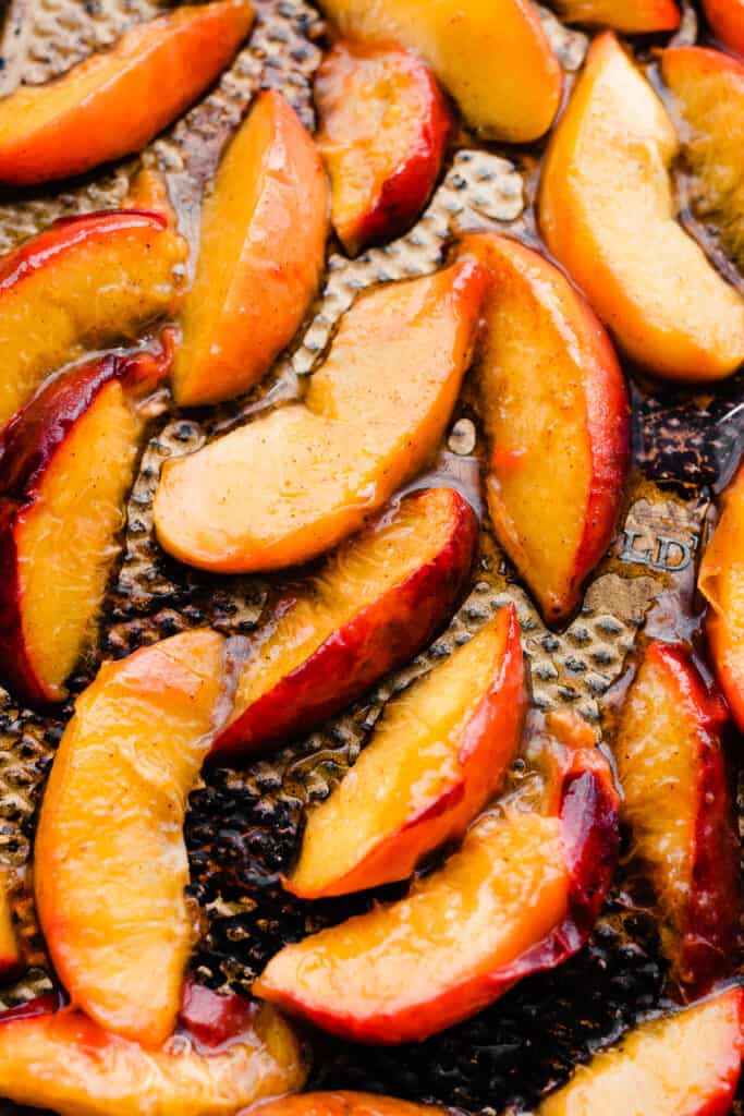 A close-up of juicy roasted peaches on a sheet pan.