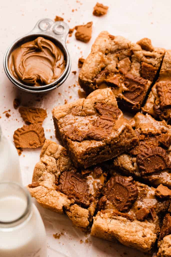 Cookie butter blondies on a light surface with bottles of milk nearby.