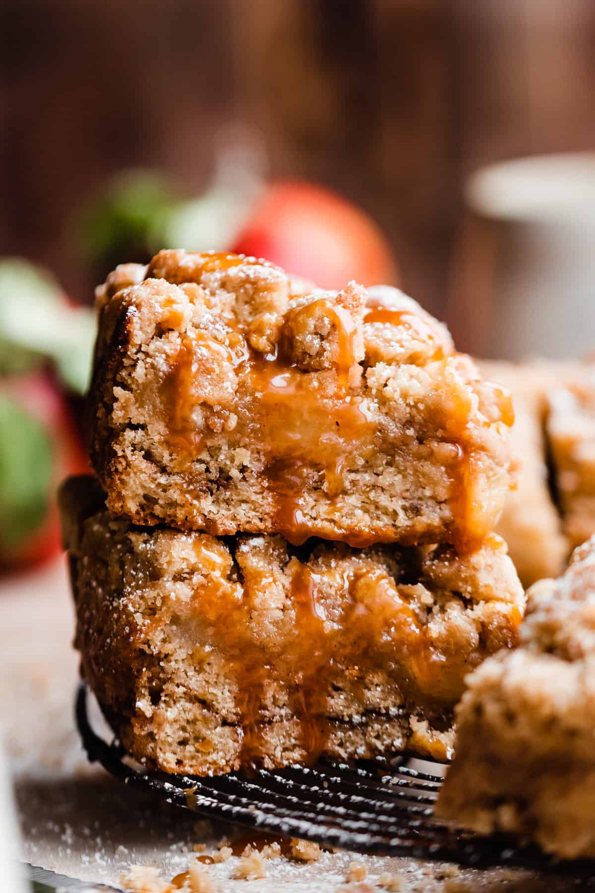 A stack of two slices of apple crumb cake drizzled with caramel, on a wire rack.