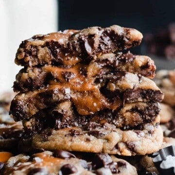 A close-up of a stack of broken open cookies with melty chocolate and gooey caramel dripping out.