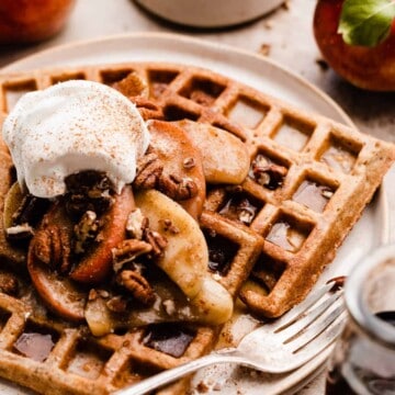 A close-up of the waffles on a plate, topped with the apples and whipped cream.