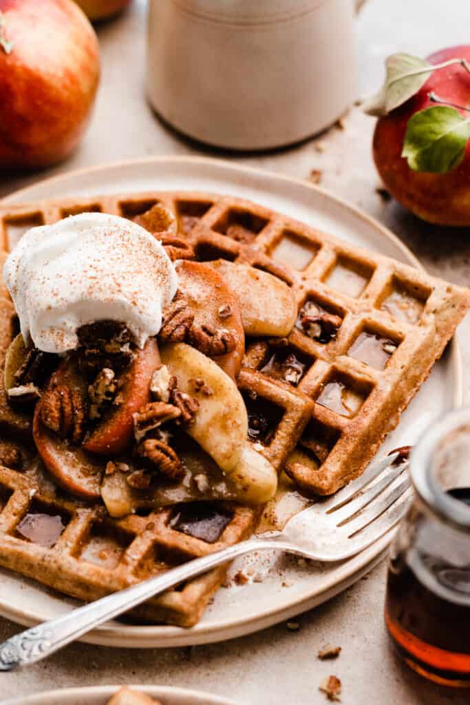 A close up of three waffles on a plate topped with caramelized apples and syrup.