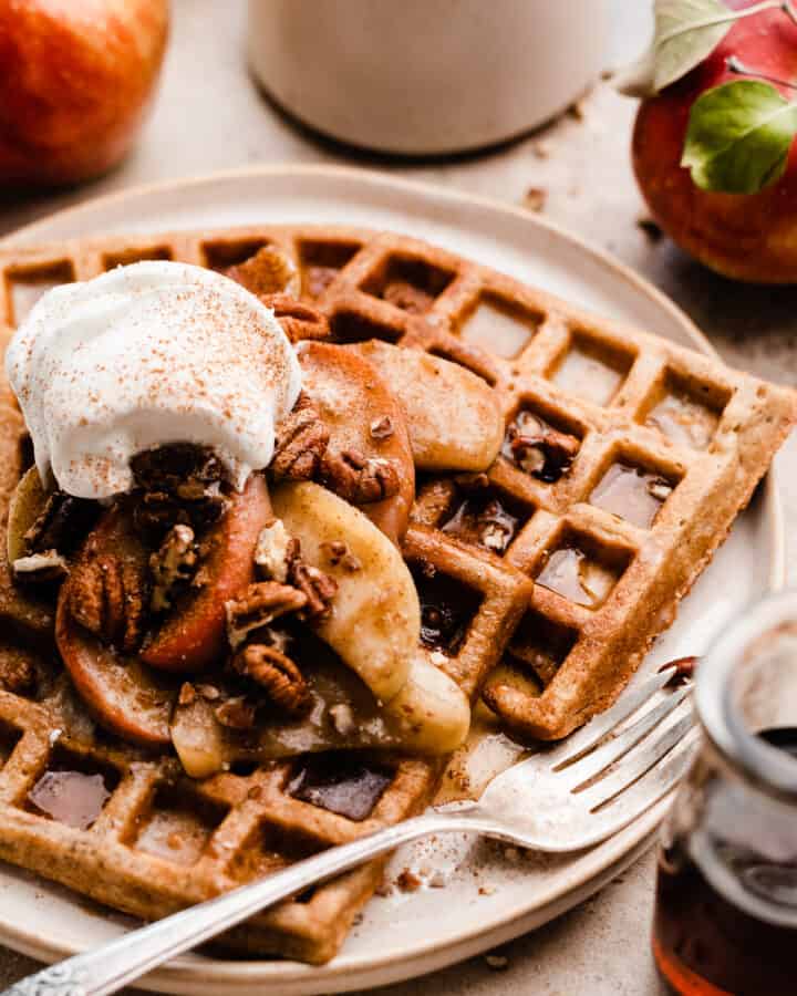 A close-up of the waffles on a plate, topped with the apples and whipped cream.