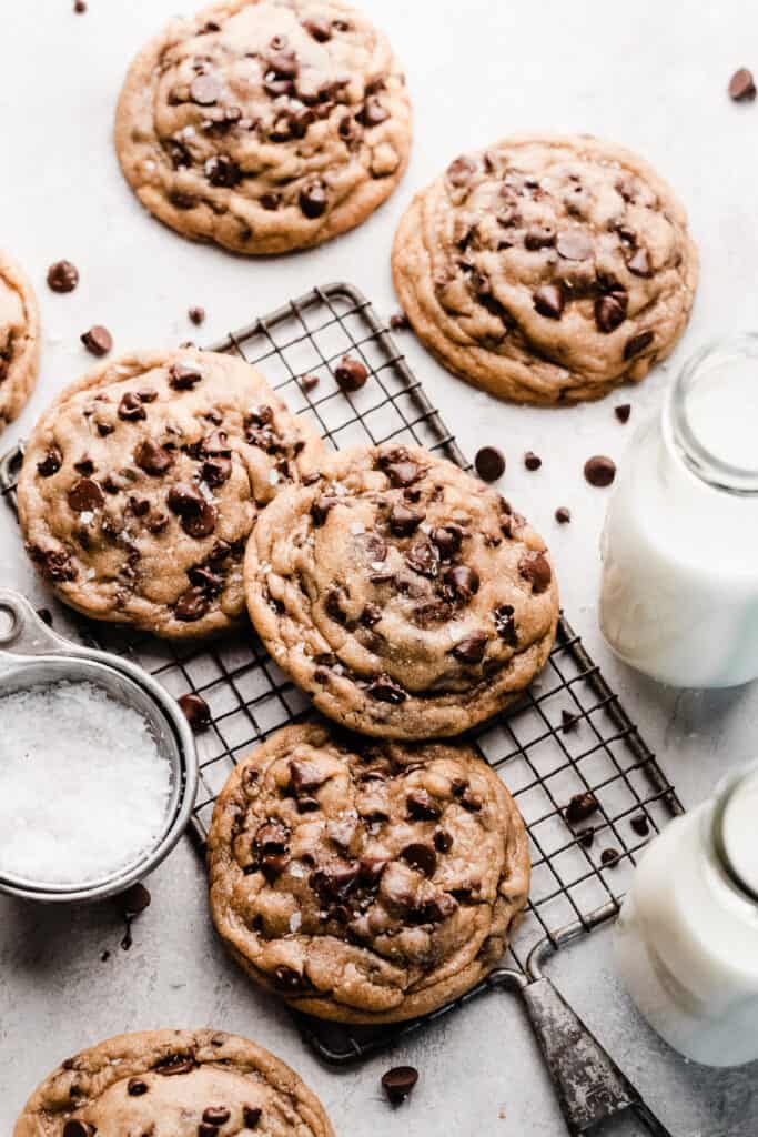 Bakery-Style chocolate chip cookies on a wire rack with milk bottles and flaky sea salt nearby.