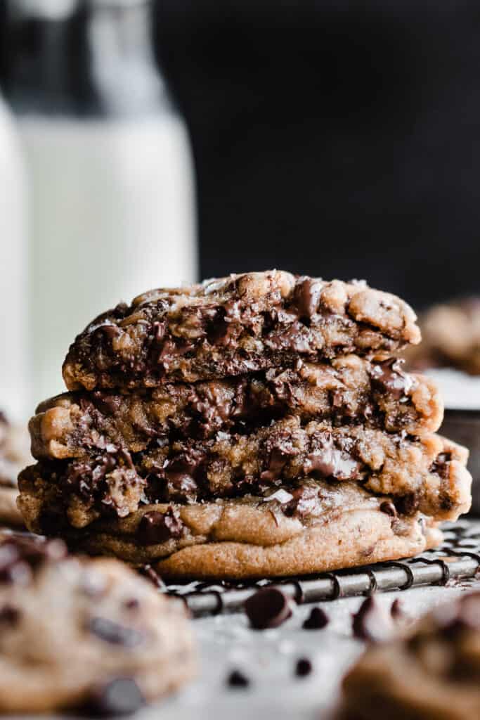 A stack of broken open chocolate chip cookies on a wire rack, revealing their gooey insides and melty chocolate puddles.