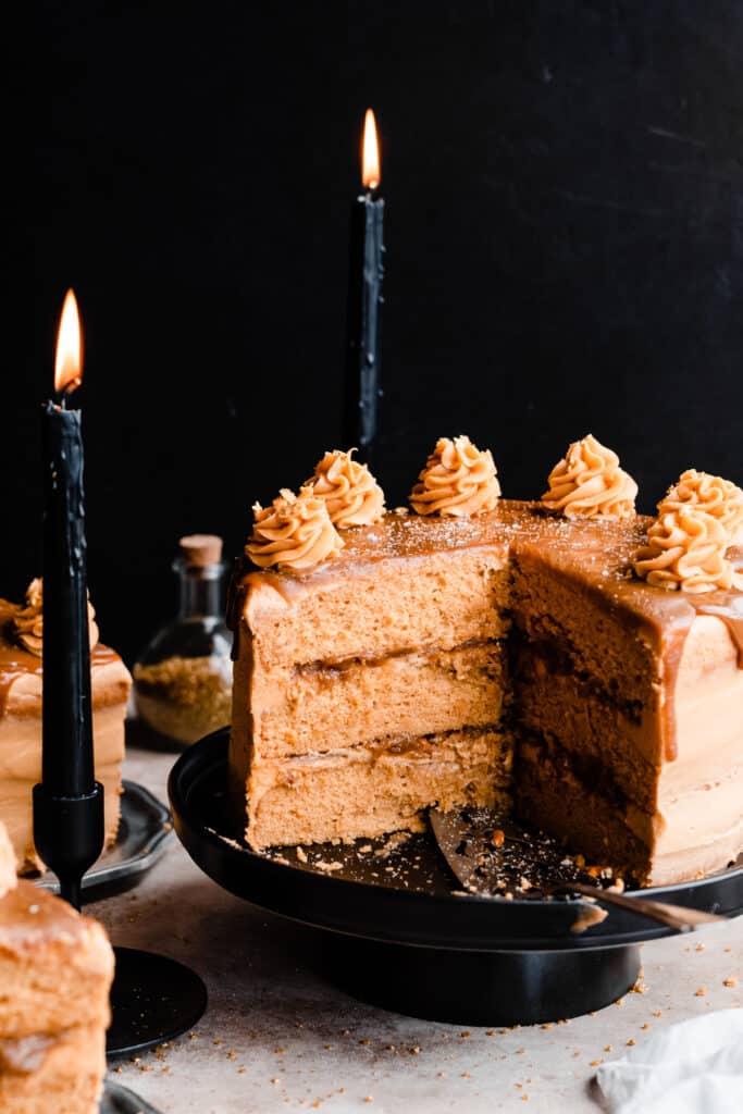 Layered butterscotch cake on a cake stand with a few slices missing, with a butterscotch drip on top and piped frosting swirls.