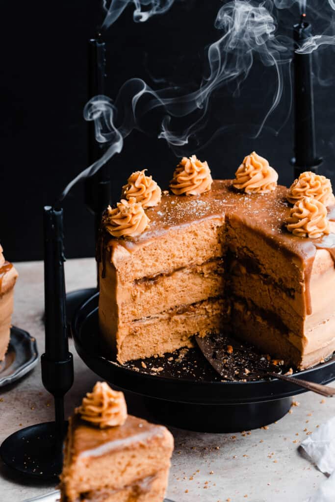 Layered butterscotch cake on a cake stand with a few slices missing, with a butterscotch drip on top and piped frosting swirls.