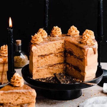 Layered butterscotch cake with a cross section missing, on a black cake stand with a butterscotch drip and frosting swirls on top.