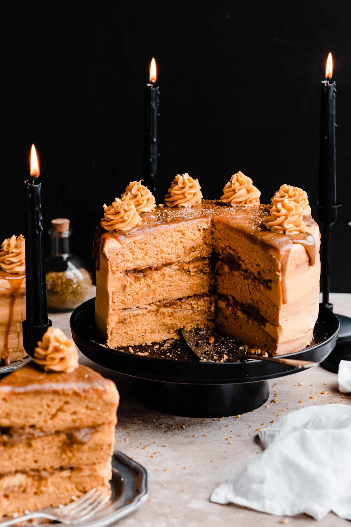 Layered butterscotch cake with a cross section missing, on a black cake stand with a butterscotch drip and frosting swirls on top.