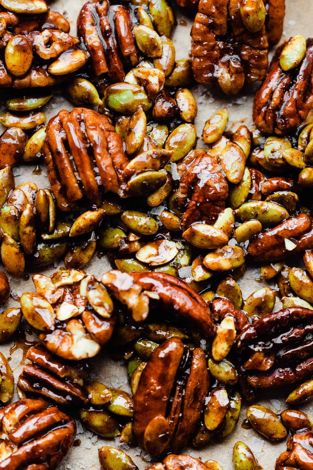 A close-up of candied pecans and pepitas on a baking sheet.