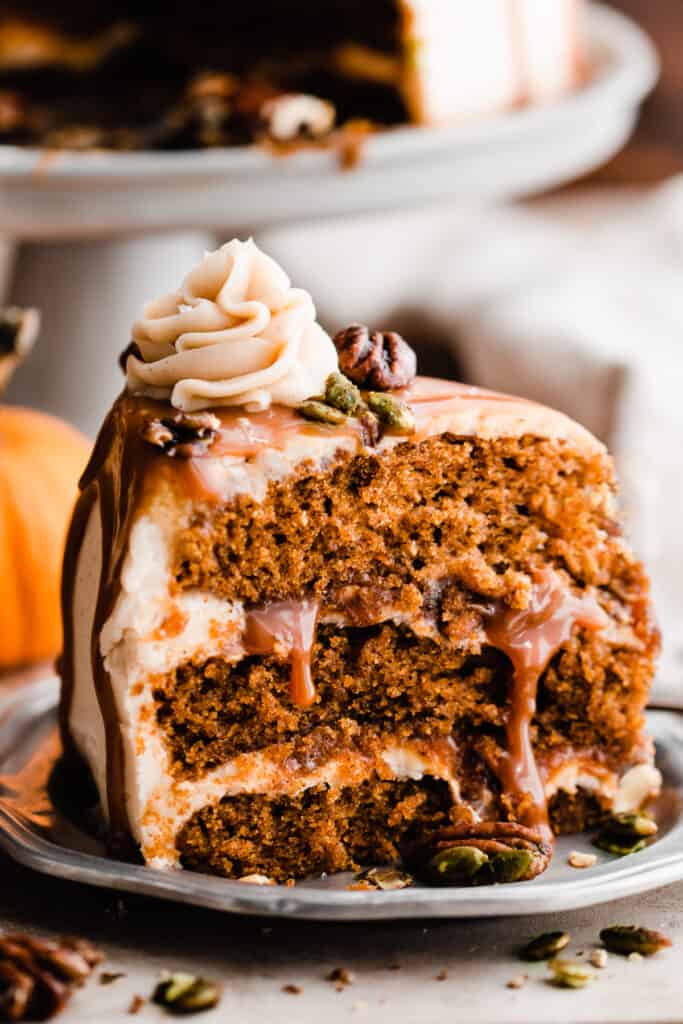 A close-up on a slice of pumpkin cake with moist layers, a caramel drip, and candied nuts.