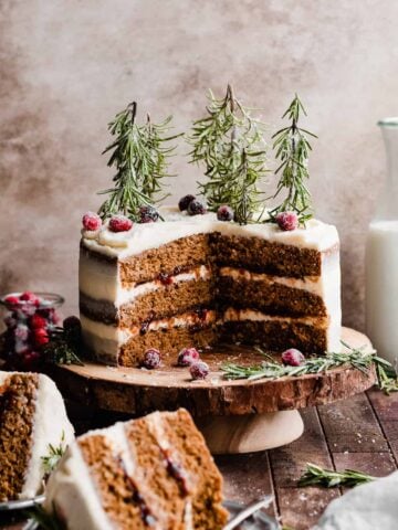 Sliced gingerbread cake on a wooden stand, with sugared cranberries and rosemary trees on top.