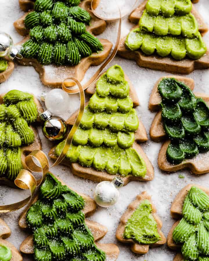 Honey cutout cookies decorated like evergreen trees on a sugary backdrop.