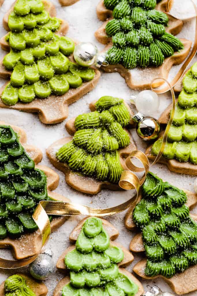 Honey cookies decorated like christmas trees on a sugary surface, with christmas ribbon and ornaments.