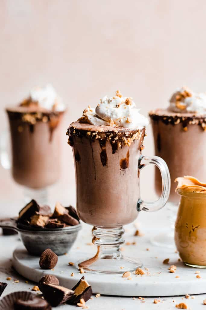 Glasses of peanut butter chocolate milkshakes topped with whipped cream and peanuts. 