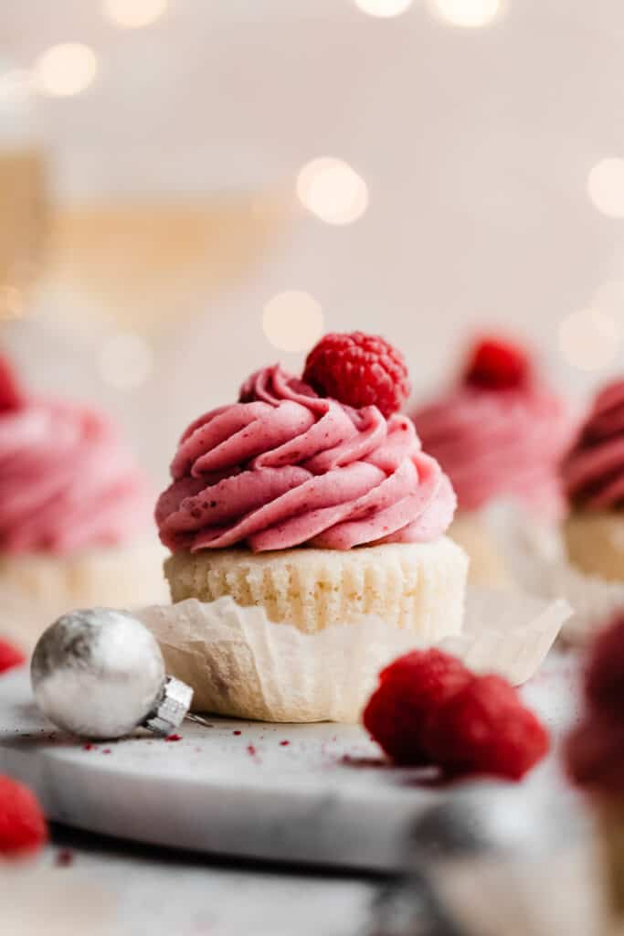 A close-up on a raspberry topped raspberry cupcake on a marble surface.