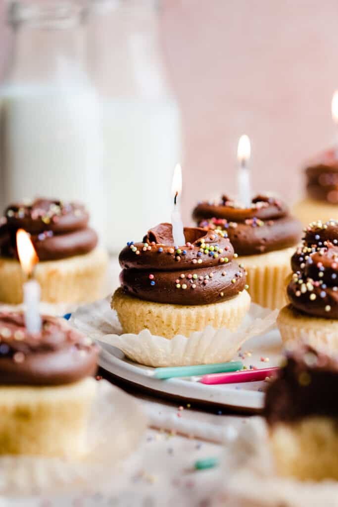 Chocolate frosted yellow cupcakes with colorful sprinkles and lit birthday candles.