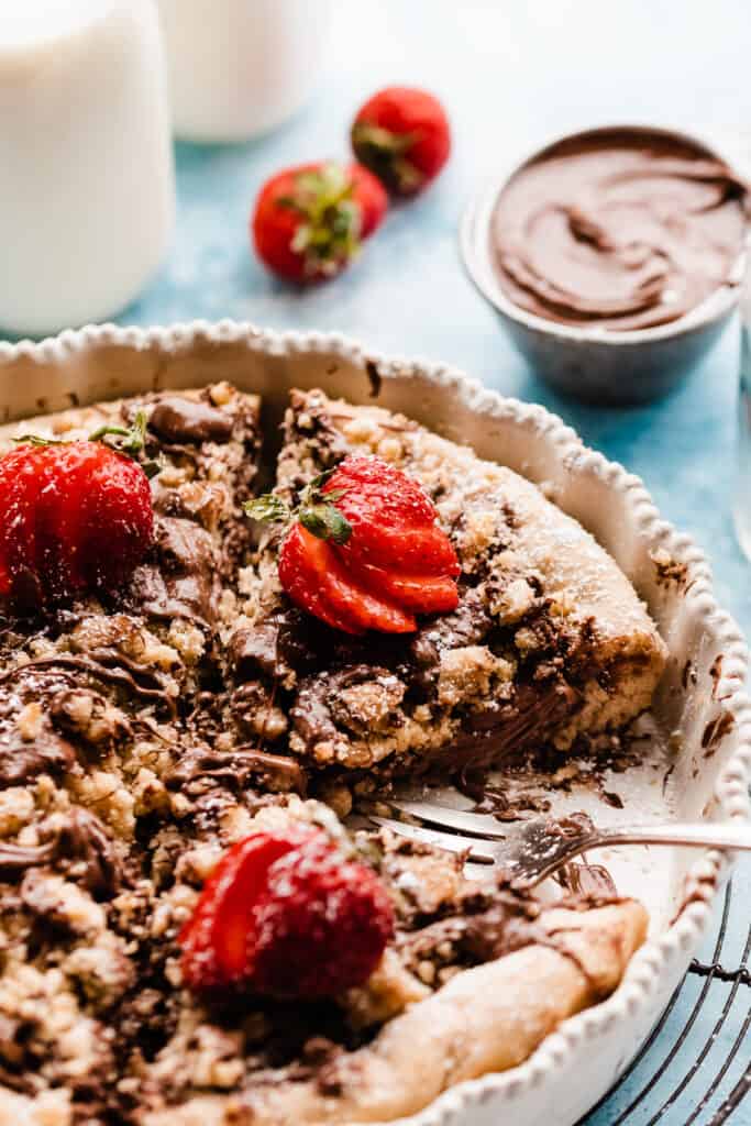 Slices of nutella pizza in a baking dish, drizzled with nutella and topped with fresh strawberries.