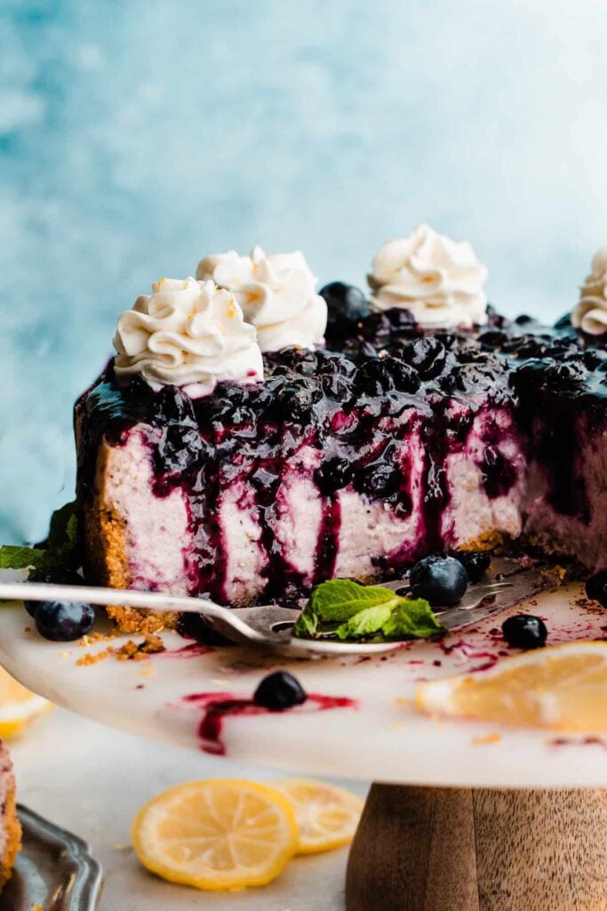 A cross-section of the sliced cheesecake on a cake stand with a visible purple inside and blueberry sauce on top.