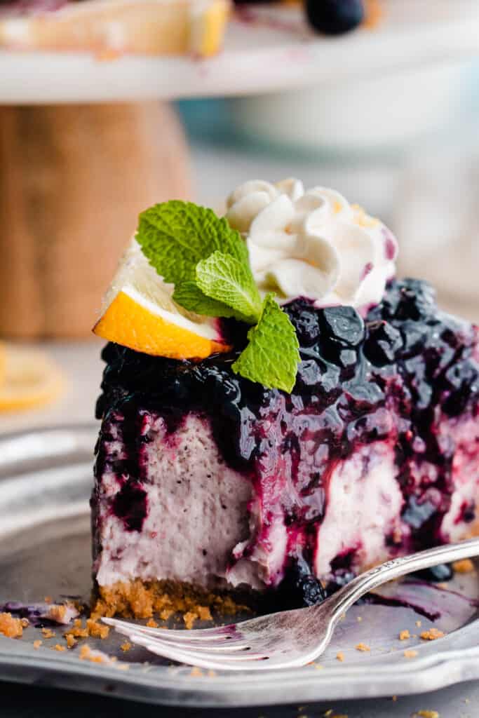 A slice of blueberry lemon cheesecake on a plate with a bite missing.