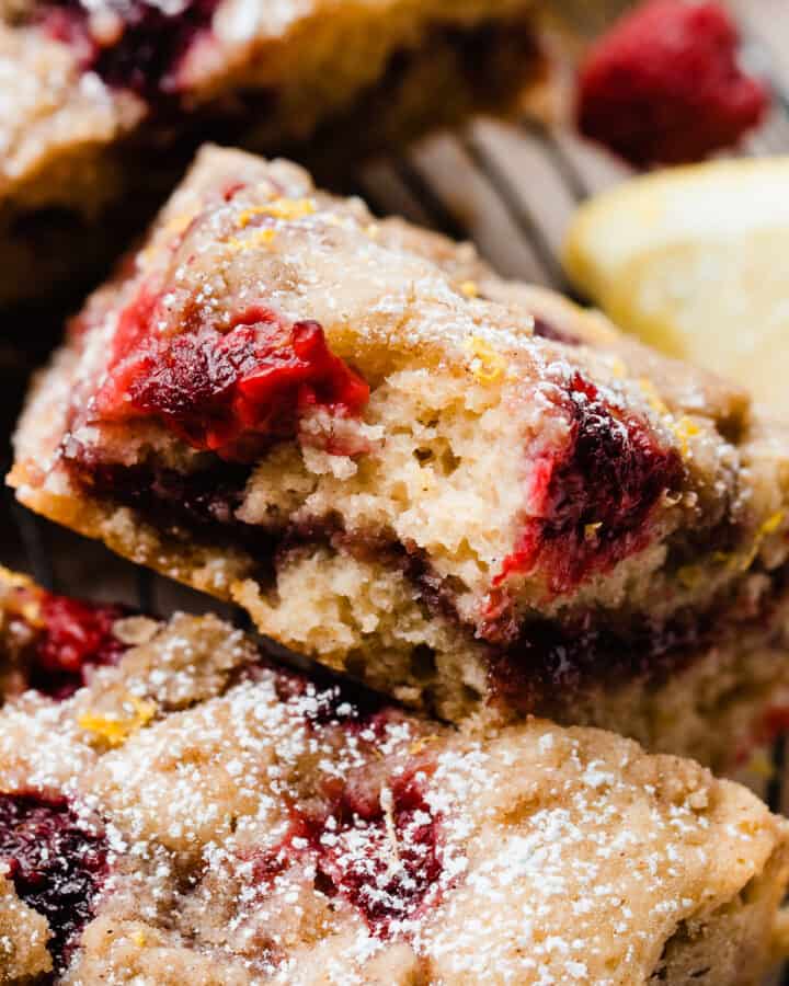 A close-up on a slice of coffee cake with a bite missing, showing the raspberry rippled center and fresh raspberries baked in.