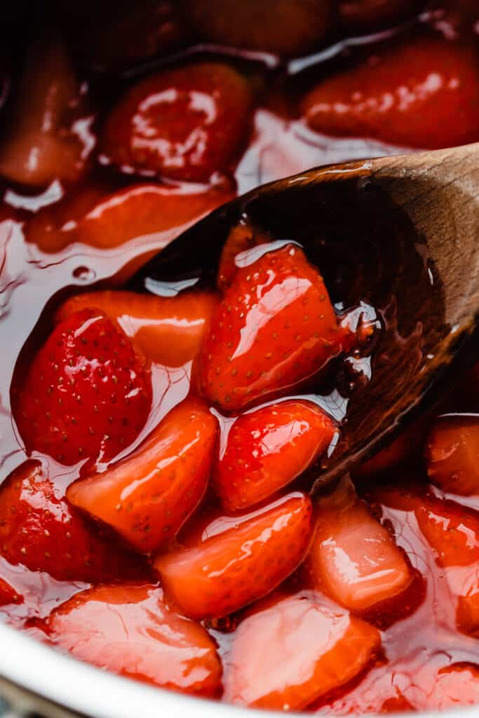A close-up of the strawberry sauce in a saucepan with a wooden spoon.